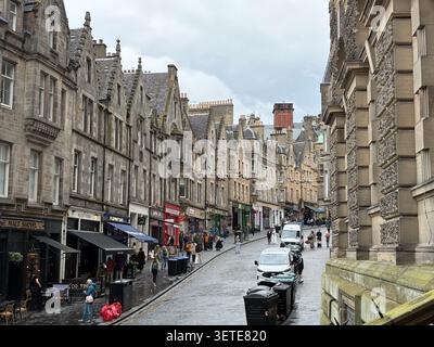 Steinhäuser und Geschäfte entlang der Royal Mile in Edinburgh, Old Town, Schottland, mit Fußgängern und Fahrzeugen auf einer nassen Straße. Stockfoto