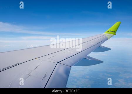 Blick aus einem Passagierfenster mit Blick auf den Flügel eines AirBaltic Airbus A220-Flugzeugs, das in großer Höhe unterwegs ist. Stockfoto
