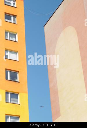 Ein minimalistisches Bild aus farbenfrohen geometrischen Wohnblöcken, die einen schmalen Streifen blauen Himmels mit einem einsamen Vogel umrahmen. Stockfoto