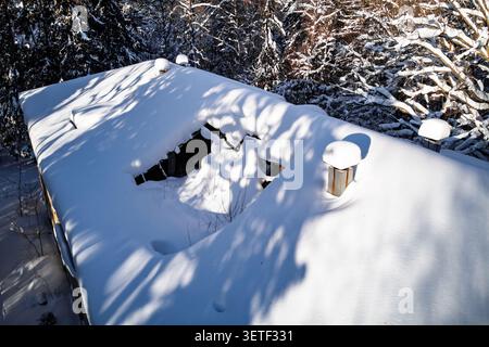 Blick aus der Drohne auf ein heruntergekommenes, schneebedecktes Dach mit klaffendem Loch, das zu einem alten verlassenen Gebäude in einer wilden Winterlandschaft gehört Stockfoto