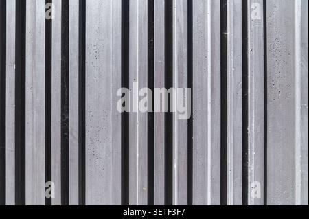 Gerillte Betonwandstruktur mit vertikalen Linien. Moderner minimalistischer architektonischer Hintergrund mit dunkelgrauer gerippter Steinoberfläche mit Streifen. Stockfoto