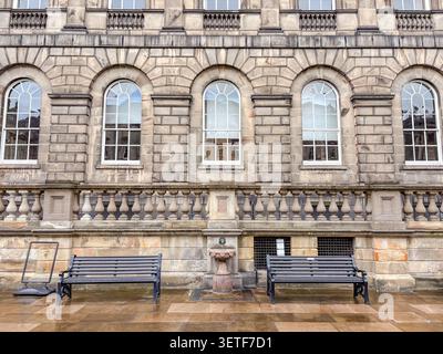 Außenansicht des Old College an der University of Edinburgh mit Sandsteinmauerwerk, Bogenfenstern und zwei Parkbänken auf einem nassen Stein plaza. Stockfoto