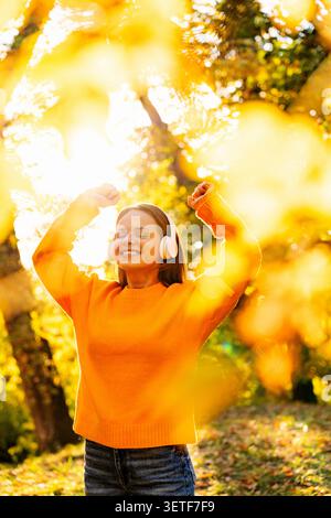 Glückliche Frau, die Musik hört, während sie im Herbstpark spaziert. Stockfoto