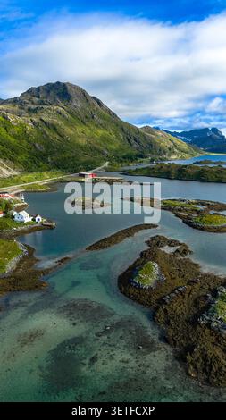 Atemberaubende Aussicht auf die Lofoten Inseln aus der Vogelperspektive mit türkisfarbenem Wasser, felsigen Inselchen, steilen grünen Bergen und traditioneller roter Hütte Stockfoto