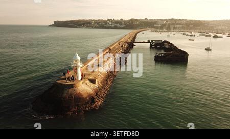 Blick aus der Vogelperspektive auf den Brixham Breakwater Lighthouse mit Menschen, die entlang des Steinbruchs spazieren, umgeben vom ruhigen Meer und den Booten im Hafen i Stockfoto