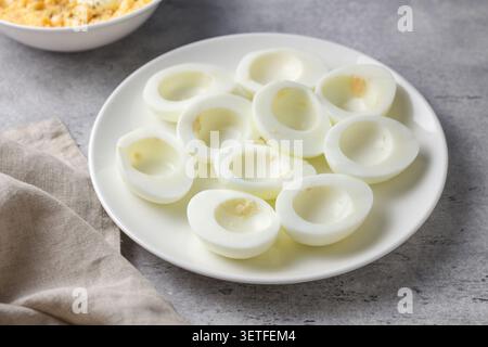 Hart gekochte Eierhälften mit Eigelb auf einer weißen Platte, zubereitet für gefüllte Eier Rezept auf einer grauen strukturierten Oberfläche mit weichem natürlichem Licht Stockfoto