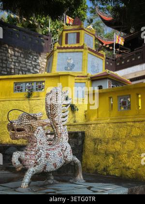 Traditionelle Mosaikstatue qilin vor einem gelben Tempelgebäude. Eine wunderschöne Mosaikskulptur einer mythischen Drachenwache Stockfoto
