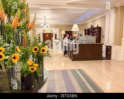 Die Rezeption des Grand Hotels und die Innenausstattung der Lobby im Balmoral Hotel mit einem Mann, der eincheckt, und lebhaften Blumenarrangements. Stockfoto