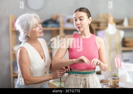 Ältere Näherin nimmt Körpermaße von erwachsenen Frauen Stockfoto
