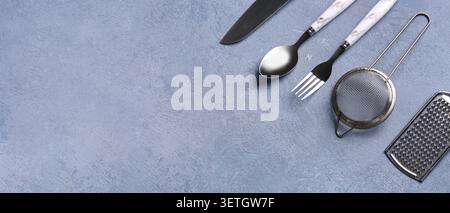 Küchenutensilien einschließlich Messer, Löffel, Gabel, Sieb und Reibe auf blauer Oberfläche Stockfoto