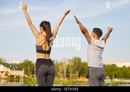Sportliche Yogi stehen aktiv im Freien, heben die Arme hoch über dem Kopf, Strecken sich Stockfoto