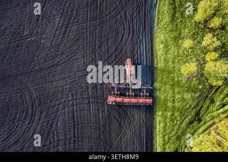 Sämaschine, die entlang der Kante des gepflügten Feldes arbeitet, mit Kopierraum, aus der Vogelperspektive auf Frühjahrspflanzen, Landwirtschaft und Pflanzenproduktion. Stockfoto