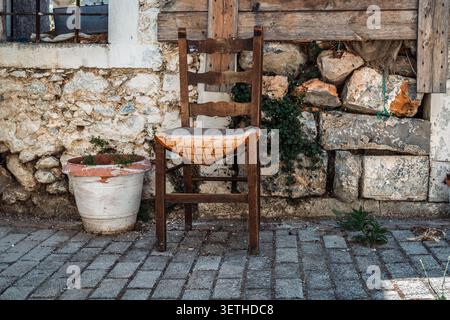 Straßenszene in einem Dorf im Osten Kretas: Ein alter Stuhl und ein Keramikblumentopf an der Wand eines alten Hauses Stockfoto