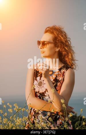 Frau Blumen Sonnenbrille, junge Frau in Blumenkleid hält eine winzige Blume bei Sonnenuntergang mit schönem natürlichen Licht Kopierraum Stockfoto