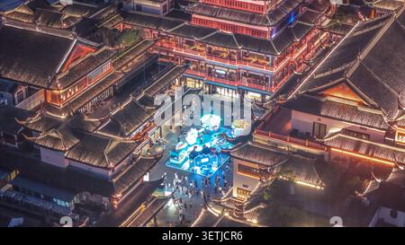 Blick aus der Vogelperspektive auf die beleuchtete traditionelle Architektur des Yu Gartens bei Nacht mit Menschen, die durch den Innenhof laufen und leuchtende Darstellungen in Shangh zeigen Stockfoto
