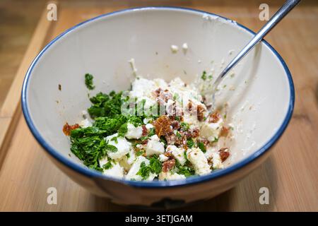 Mischen Sie Feta, sonnengetrocknete Tomaten und viel Petersilie in einer Schüssel, um einen aromatischen Dip für eine Sommerparty zu machen, ausgewählten Fokus, enge Tiefe des Fie Stockfoto