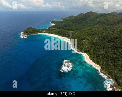 Ozean mit stürzenden Wellen gegen felsige Ausläufer entlang des Strandes. Seychellen, Mahe. Stockfoto