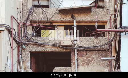 Unordentliches Gewirr von elektrischen Kabeln und Rohren an einer alten Gebäudefassade Stockfoto