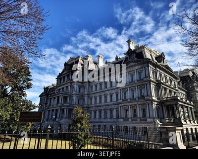 Ein Seitenblick auf das Dwight D. Eisenhower Executive Office Building, leer von Menschen, an einem hellen, sonnigen Tag, eingerahmt von Parkbäumen. Stockfoto