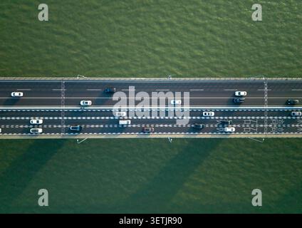 Blick von oben nach unten auf den Straßenverkehr fließt in beide Richtungen auf einer breiten Brücke, die einen Fluss überspannt. Hangzhou, China. Stockfoto