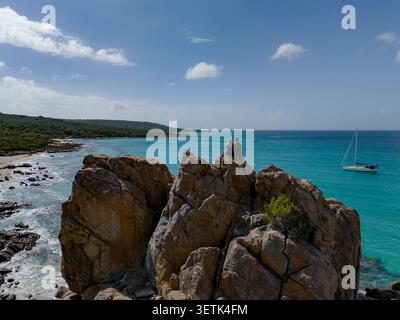 Blick aus der Vogelperspektive auf Castle Rock mit zwei Personen auf der Granitformation mit Blick auf türkisfarbenes Wasser, ein Segelboot und die Küste von Dunsborough Stockfoto