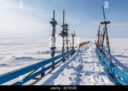 Blick auf Goryachiye Istochniki Khakusy mit hölzernen Wegweisern auf einem schneebedeckten Pier, der auf die gefrorene Oberfläche des Baikalsees in Severobaykalskiy führt Stockfoto