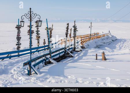 Blick auf Goryachiye Istochniki Khakusy mit hölzernen Wegweisern und blauem Geländer auf einem schneebedeckten Pier mit Blick auf den gefrorenen Baikalsee im Severobaykal'skiy Rayon Stockfoto