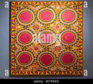 Lebendige traditionelle Suzani-Stickerei mit neun runden Medaillons und komplizierten Blumenmotiven in kräftigen Gelb-, Rosa- und Blautönen. Ideal für Kubikmeter Stockfoto