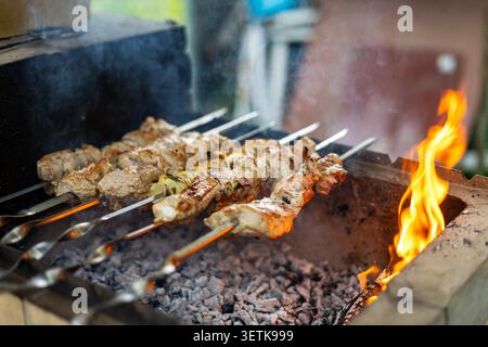 Gegrillte Schweineköpfe über Holzkohlegrill-Flammen. Schweinekebabs grillen über heißer Holzkohle in einem Grill im Freien, wobei Rauch aus dem gebräunten Fleisch steigt Stockfoto