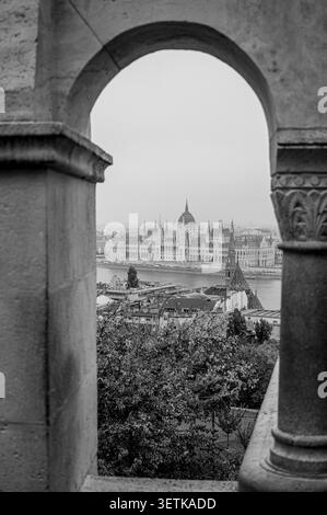 Schwarz-weiß-Blick auf das ungarische Parlamentsgebäude, eingerahmt durch einen Steinbogen an der Fischerbastei in Budapest, Ungarn. Stockfoto