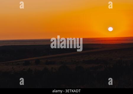 Leuchtend orangefarbener Sonnenuntergang über den sanften Hügeln und landwirtschaftlichen Feldern in der Nähe des Donautals in Russe, Bulgarien. Stockfoto