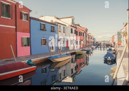 Blick auf farbenfrohe Häuser und kleine Boote, die an einem ruhigen Kanal an einem sonnigen Tag in Burano, Italien, ankern. Stockfoto