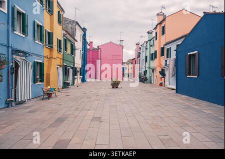 Breite gepflasterte Straße, umgeben von bunt bemalten Wohnhäusern an einem bewölkten Tag in der Inselstadt Burano, Italien. Stockfoto
