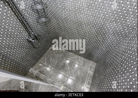 Eine stilvolle Dusche mit grauen Mosaikfliesen, Marmorfliesen und moderner Duschausstattung. Das schlanke Design ist optisch beides Stockfoto
