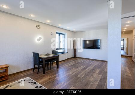 Elegantes Wohnzimmer mit Holzfußboden, Essbereich, Fernseher und moderner Beleuchtung. Die Farbpalette ist hauptsächlich weiß und braun Stockfoto