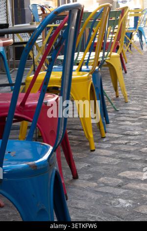 Lebhafte Tolix-Metallstühle in einer Reihe in einer bezaubernden Kopfsteinpflasterstraße, die in einem Café oder einer Restaurantterrasse im Freien in einer Stadt auf Gäste warten Stockfoto