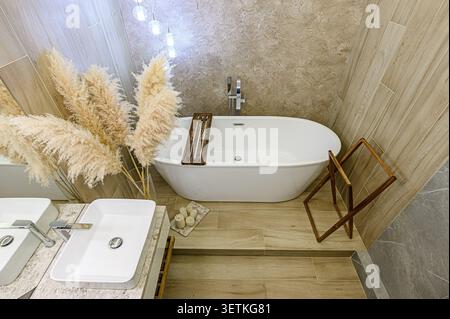 Ein stilvolles Badezimmer mit freistehender Badewanne, zwei Waschbecken, neutralen Fliesen und dekorativem Pampasgras für eine ruhige, Spa-Atmosphäre Stockfoto