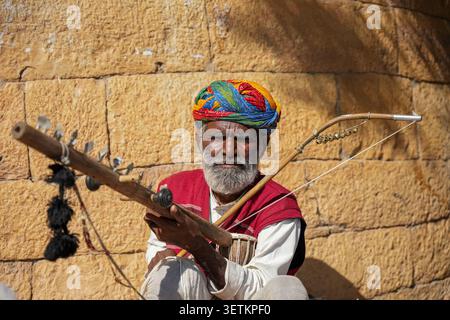 Rajasthani Volksmusiker Spielt Traditionelles Streichinstrument In Der Nähe Der Sandsteinmauer Stockfoto