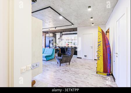 Ein offener Wohnbereich mit einem Wohnbereich mit blauem Sofa, Sessel und einer Küche im Hintergrund, beleuchtet mit Deckenleuchten Stockfoto