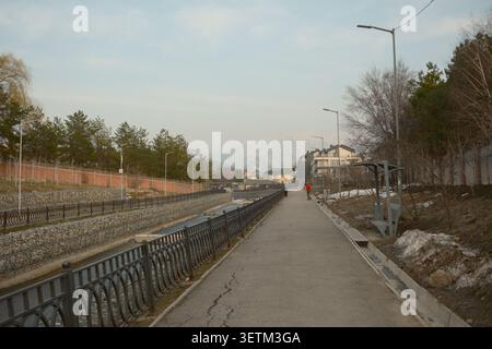 Langer Fußgängerweg entlang eines Flussufers. Konzept des Gehens, gesunder Lebensstil, Outdoor-Bewegung, Stadtplanung und friedliches Stadtleben. Stockfoto