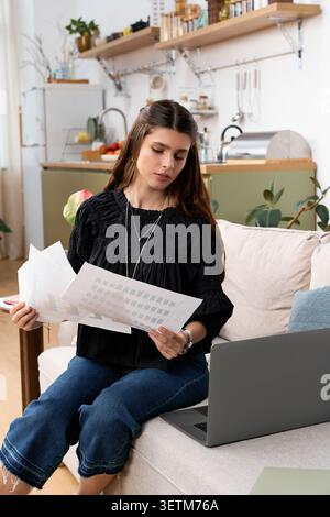 Eine junge Frau arbeitet fernab von ihrer stilvollen Wohnung, Papiere in der Hand Stockfoto