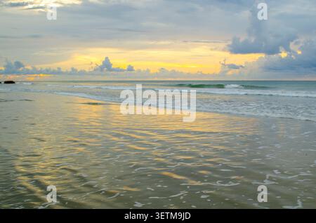 Panorama des Sonnenuntergangs an der Küste mit warmem goldenem Licht, das sich auf flachen Gewässern unter Schichten von Wolken reflektiert Stockfoto