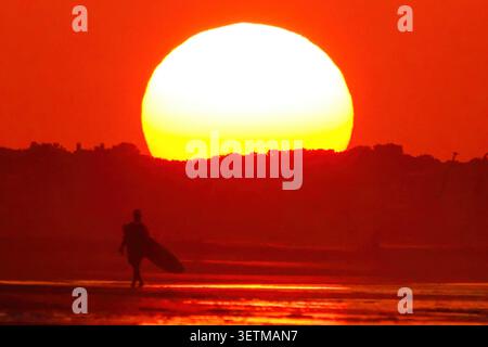 Isle Of Palms, Usa. Juni 2026. An einem heißen Morgen in The lowcountry, 23. Juni 2026 in Isle of Palms, South Carolina, spaziert ein Surfer am Strand entlang. Quelle: Richard Ellis/Richard Ellis/Alamy Live News Stockfoto
