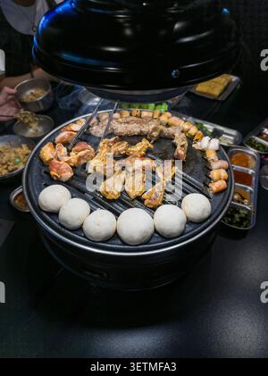 Eine lebhafte koreanische Grillszene mit einer Auswahl an gegrillten Meeresfrüchten und Fleisch auf einem runden Grill. Die rauchige Atmosphäre unterstreicht das kochende Essen, gratis Stockfoto