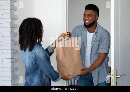 Lieferung Von Lebensmitteln. Lächelnder schwarzer Kurier, der Auftrag zum Haus der jungen Frau liefert Stockfoto