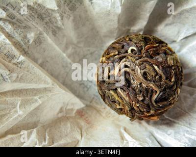 Komprimierter Pu-erh-Teekugel in traditionellem Papier. Nahaufnahme chinesischer Teehandwerkskunst und natürliche Teeblätter-Textur. Stockfoto
