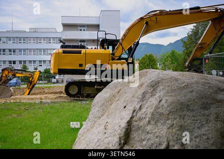 Gelber Bagger, der auf einer städtischen Baustelle mit einem großen Felsen im Vordergrund arbeitet. Stockfoto