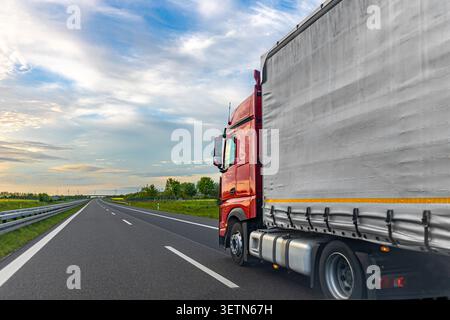 Roter Lastwagen auf der Autobahn. Güterverkehrsszene mit offener Straße. Stockfoto