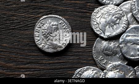 Eine Nahaufnahme von oben auf alte römische Silbermünzen auf einer dunklen, stark strukturierten rustikalen Holzoberfläche. Eine Münze mit dem Profil eines Stockfoto