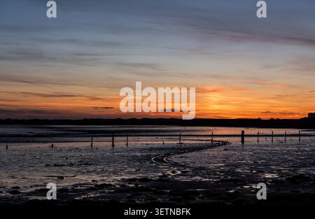 Sonnenuntergang hinter Dünen an der Westküste Englands; feuchtes Wattenmeer im Vordergrund reflektieren das untergehende Sonnenlicht; Fechtpfosten und Reifenspuren hervorgehoben Stockfoto